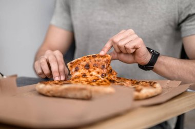 Piece of pizza. Mens neat hands taking piece of fresh appetizing pizza lying in box on table no face