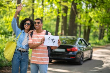 Hitchhiking. Smiling couple standing on the road and waiting for the car