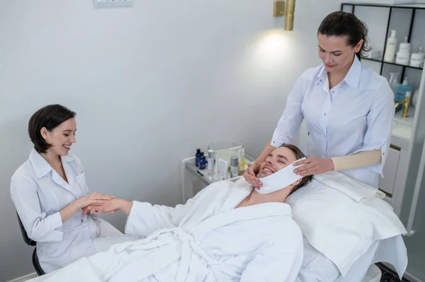 Skin care. Young man having hand massage and face procedures in the salon