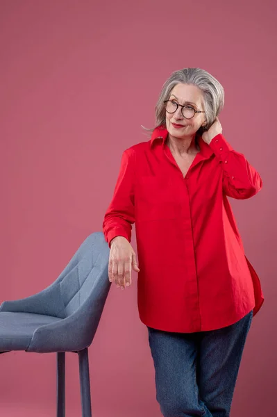 Studio Mature Woman Red Shirt Eyeglasses Standing Chair — Zdjęcie stockowe