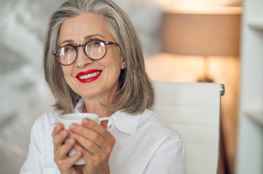 Coffee break. Elegant mature woman having coffee and looking peaceful