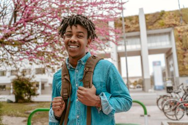Good day. Happy african guy with backpack looking at camera confidently standing on city street on warm day
