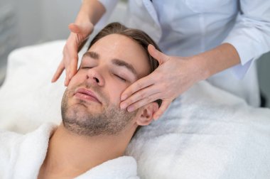 Face massage. Female professional doing face massage to a male client