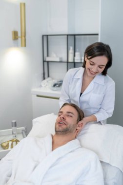 Face care. Dark-haired professional doing face massage to a male customer