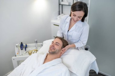 Face care. Dark-haired professional doing face massage to a male customer