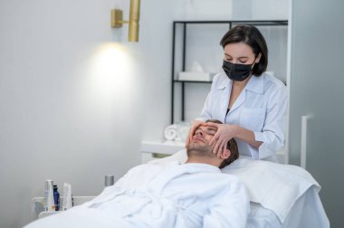 Beauty procedures. Female specialist in a protective mask working with a customer in a beauty salon