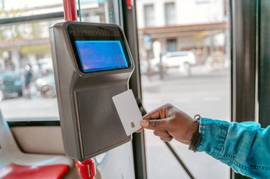 E-ticket. Dark-skinned male hand holding fare card near reader in city bus on fine day no face
