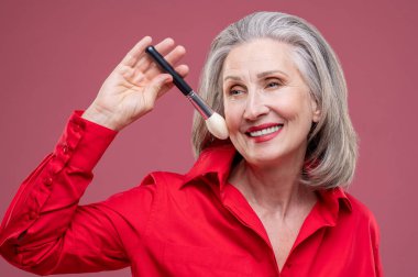 Professional makeup. Smiling woman in red with a face brush in hand