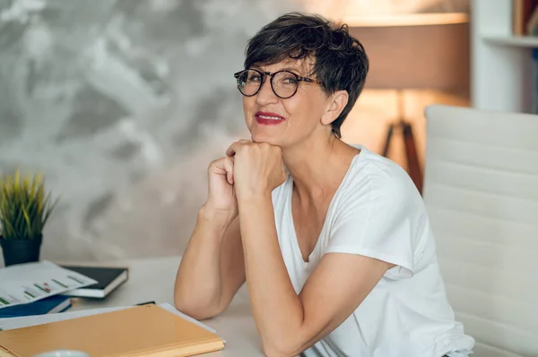 In the office. Dark-haired woman in eyeglasses sitting at the table in the office
