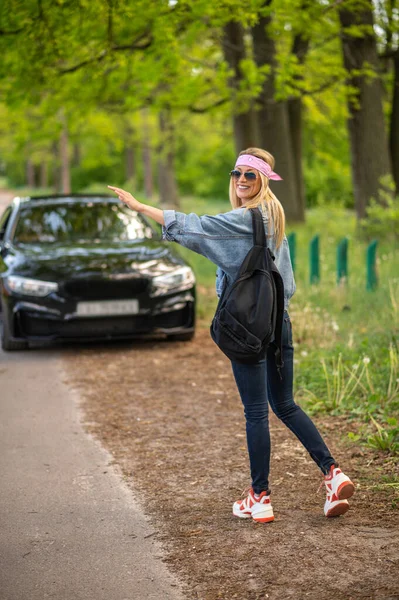 Hitchhiking. Blond young woman hitchhiking on the forest road