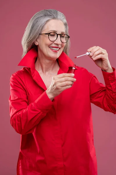 Makeup Woman Red Bright Shirt Holding Lip Gloss Looking Contented — Zdjęcie stockowe