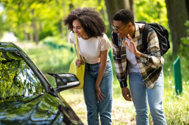 On the way to the city. Dark-skinned couple looking excited while hitchhiking on a countryside road