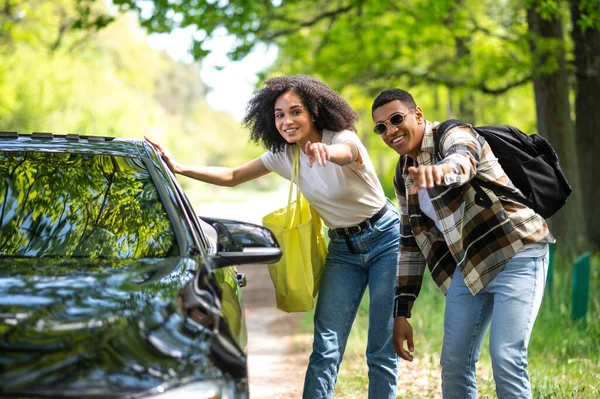 On the way to the city. Dark-skinned couple looking excited while hitchhiking on a countryside road