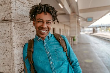 Optimism. Cheerful stylish african guy smiling at camera standing on street at railway station on fine day