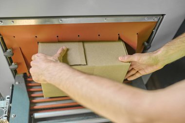Cropped photo of operator hands putting the cardboard box on the conveyor rollers of the carton sealing machine
