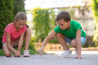 Painting. Serious focused primary school age boy and girl drawing with crayons in park on warm day