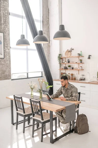 Sad young military man sitting at the table and holding a picture in his hands