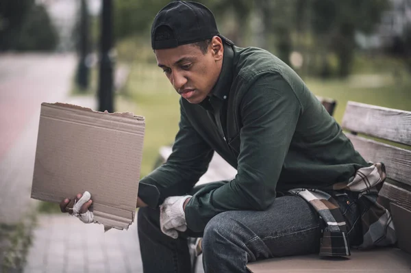 Hopelessness Dark Skinned Young Unemployed Man Holding Cardboard Sitting Park — Stock Fotó