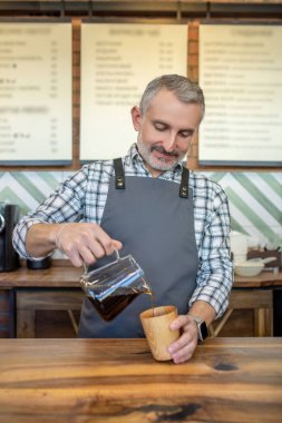 Coffee time. Barista pouring coffee to the coffee mug and looking contented