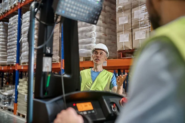 Serious Focused Warehouse Supervisor Helmet Standing Front Forklift Looking Upward — Stock Fotó