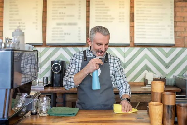 For cleaning. Man in plaid shirt and apron hoding a spray
