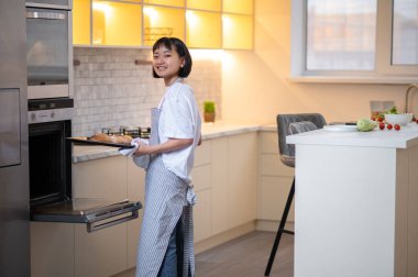 Baking pasrty. Young housewife baking something in the oven and looking busy