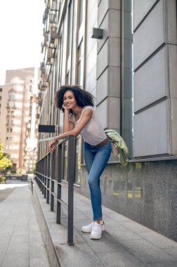 Waiting . A curly-haired young woman standing in the street near the building