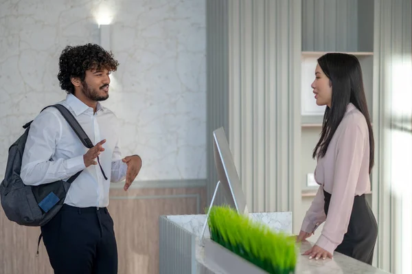 New comer. Indian young man with backpack talking to a girl on reception