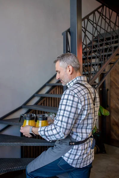 Cafe worker in the apron walking upstairs with the tray with the jugs of orange juice