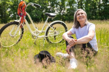 Peaceful morning. A mature woman sitting on the grass and looking peaceful