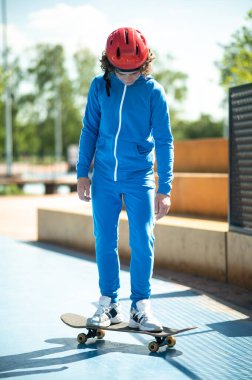 Full-size portrait of a boy in a protective helmet and sports suit standing with his both feet on the skateboard