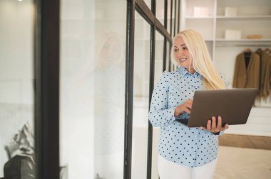 Near the window. Cute woman with laptop standing near the window