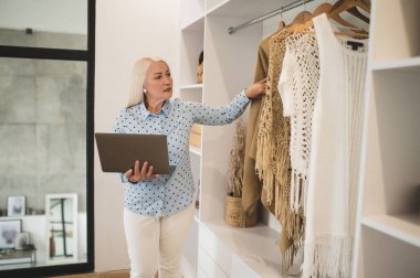 Fashionista. Cute woman with laptop choosing clothes