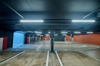 Tavanda doğrusal floresan lambalar ve yerde beyaz işaretler olan boş bir otopark.