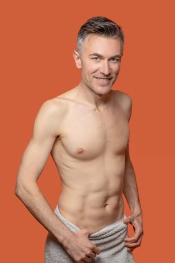 Duştan sonra. Kalçasında havluyla gülümseyen bir adam.