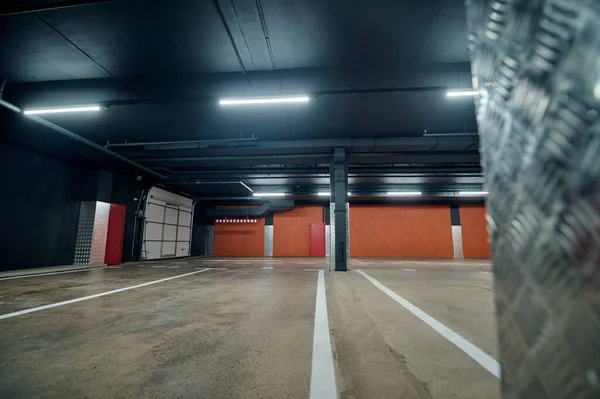 Doğrusal floresan lambalar ve beton zeminde beyaz işaretler olan bir otoparkın içinde.
