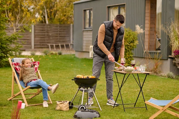 Joyous Teenage Girl Seated Garden Chair Watching Her Father Cooking — Stock Photo, Image