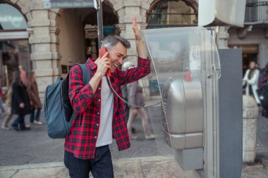 Sokakta. Ekose gömlekli adam sokak telefonunda konuşuyor.