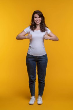 Hepsi mükemmel. Gündelik giysiler içinde güzel beyaz bir kadın fotoğraf stüdyosunda dikilirken kameraya gülümsüyor.