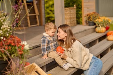 Elinde balkabağı olan mutlu bir anne verandada çocuğunun yanında oturuyor.