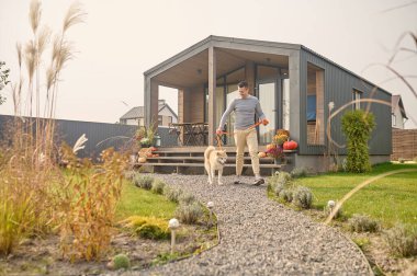 İtaatkar köpeğiyle bahçede yürüyen gülümseyen neşeli bir adamın tam boy portresi.