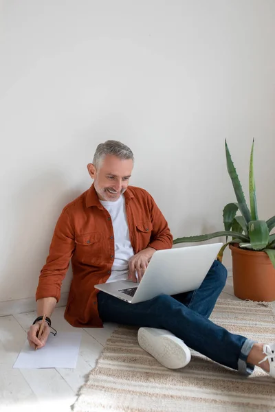 Working on project. A bearded man in terracotta shirt working on the project and looking involved