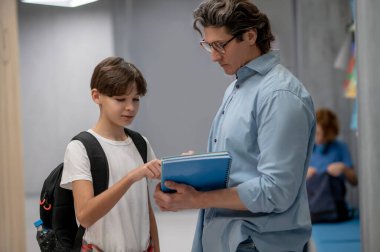 Dersten sonra öğretmeniyle iletişim kuran ciddi bir öğrencinin belden yukarı portresi.