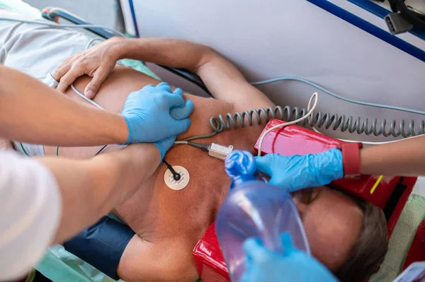 Experienced paramedics in disposable sterile gloves carrying out the cardiopulmonary resuscitation on the critical male patient