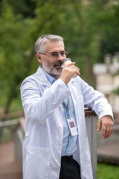 Coffee pause. Mature doctor having a break and having coffee outside