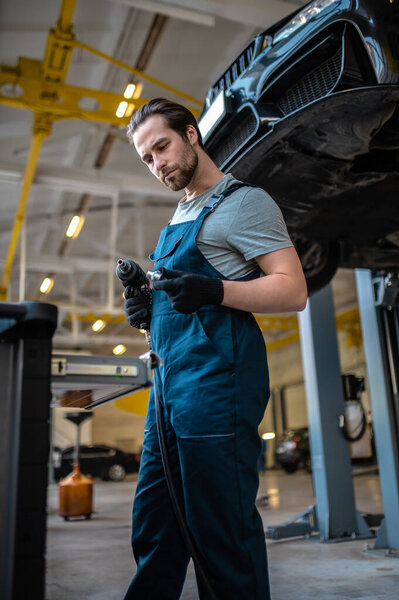 Serious automobile service technician with the drill in his hands standing before an open tool drawer