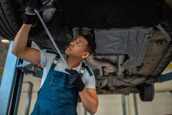 Focused young car repair technician tightening the nut on the automotive wheel with a spanner