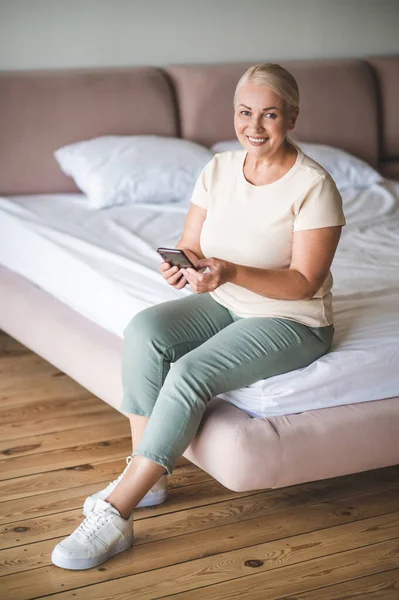 Lächelnde Schöne Blonde Dame Sitzt Auf Dem Bett Und Hält — Stockfoto