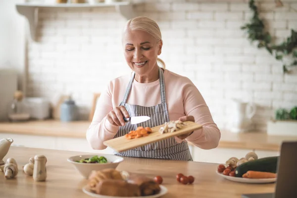 Aufgewecktes Porträt Einer Fröhlichen Hausfrau Der Schürze Die Geschnittene Möhren — Stockfoto