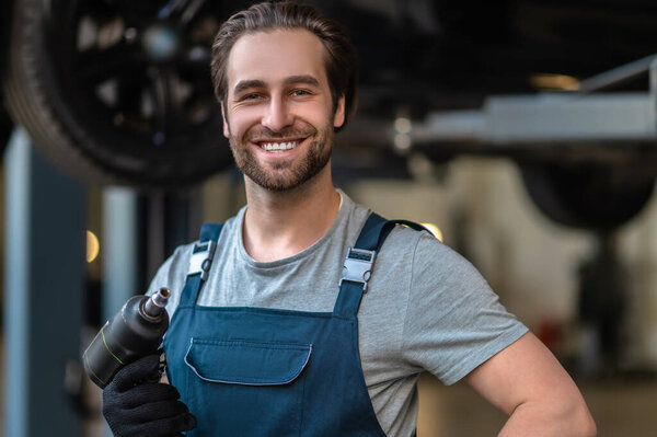 Portrait of a cheerful auto technician posing for the camera with the drill in his hand